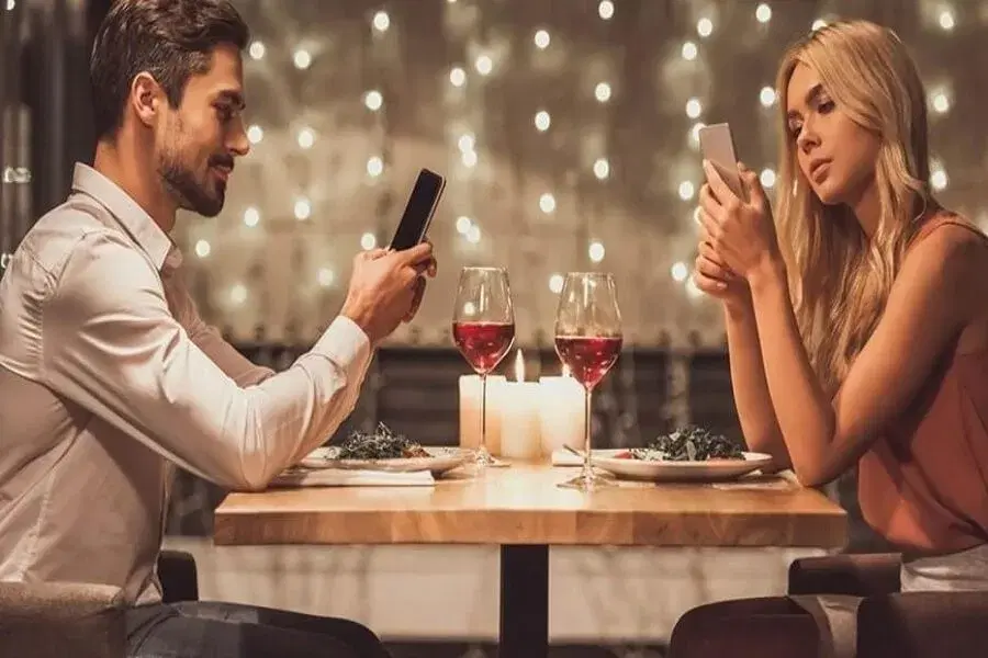 A couple at a candlelit restaurant table, each looking at their own phone.